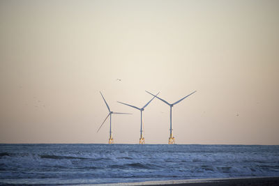 Wind turbines by sea against sky during sunset