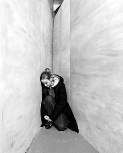 Full length of young woman sitting against wall
