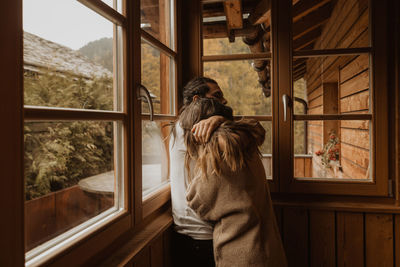 Rear view of woman looking through window at home