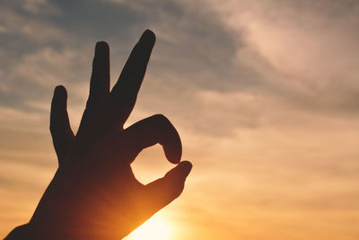 Close-up of silhouette hand gesturing against sky during sunset