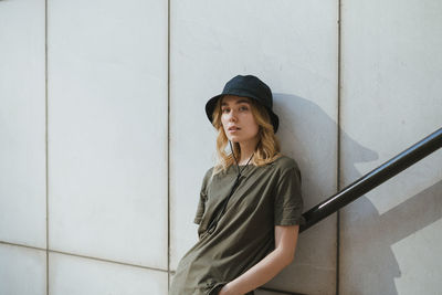 Young woman looking away while standing against wall