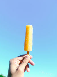 Close-up of hand holding ice cream against blue background
