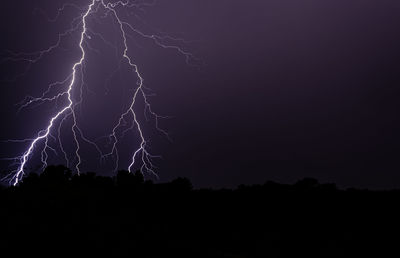 Lightning over silhouette field against sky at night