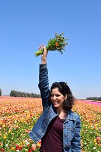 Portrait of smiling woman holding flowers against clear sky