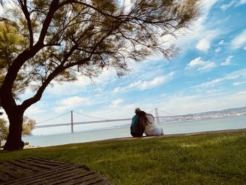 Man sitting on grass by sea against sky