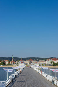 Road by river and buildings against clear blue sky