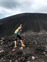 Side view of woman climbing mountain against sky