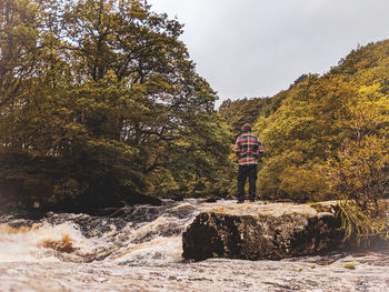 Rear view of man standing by waterfall against sky