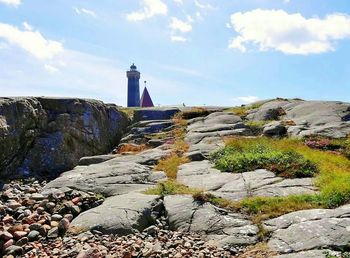 Lighthouse amidst rocks and buildings against sky