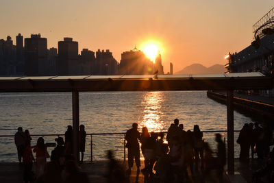 Silhouette people in city against sky during sunset