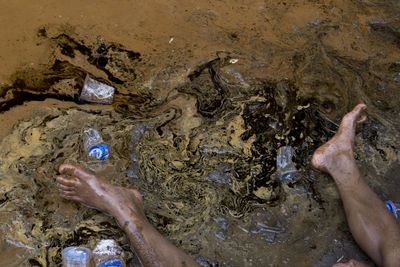 Low section of man sitting by disposable cups on wet sand