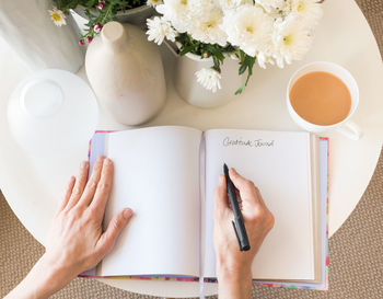 Cropped hands of woman writing in diary by coffee on table at home