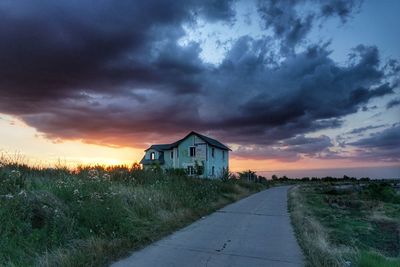 Abandoned built structure by road against dramatic sky