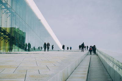 People walking on modern office building against sky