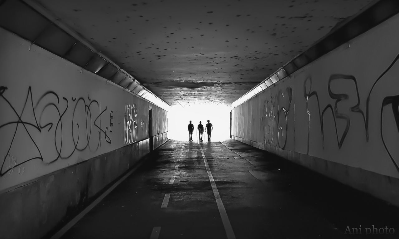 architecture, real people, text, direction, graffiti, wall - building feature, the way forward, lifestyles, indoors, tunnel, walking, women, built structure, illuminated, group of people, subway, western script, men, diminishing perspective, day, ceiling, light at the end of the tunnel, underground walkway