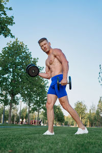 Full length of shirtless man sitting by plants against clear sky