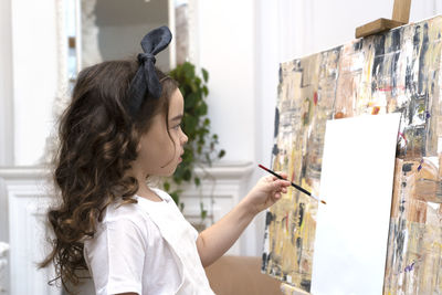 Dreamy pretty kid girl with paintbrush near drawing easel. little painting artist.