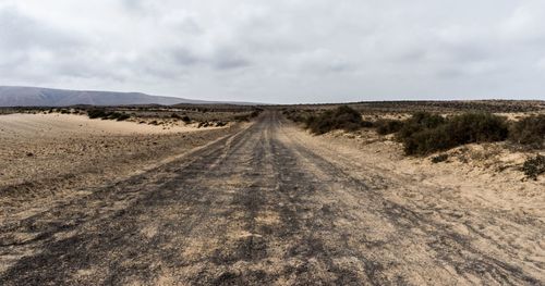 Tire tracks on sand road against sky