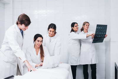 A group of doctors working on a laptop while two female doctors examine an x-ray in a white hospital room