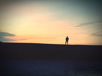 Silhouette man standing on beach against sky during sunset