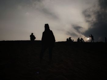 Silhouette people on land against sky at sunset