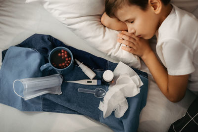Sick child sleepping on bed. nearby there are tray with medicines, fruit drink, medical mask 