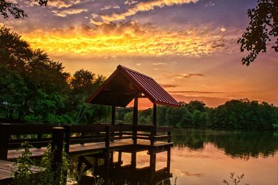 Gazebo by lake against sky during sunset