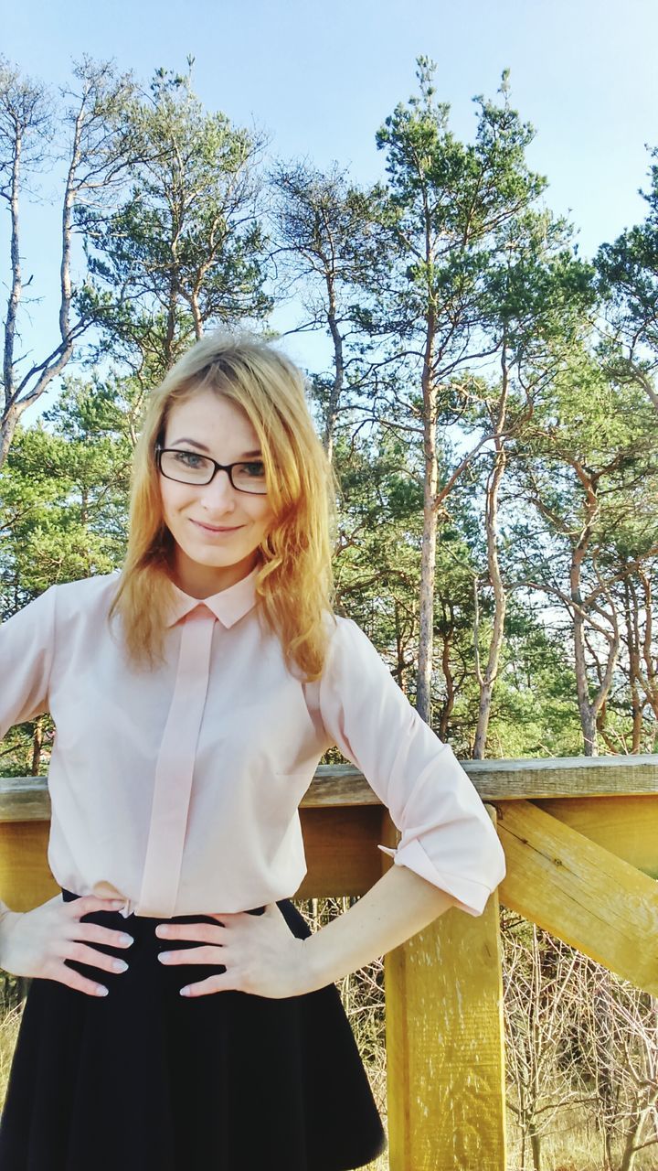 person, young adult, young women, tree, lifestyles, casual clothing, long hair, leisure activity, portrait, looking at camera, waist up, front view, smiling, three quarter length, standing, park - man made space, sitting