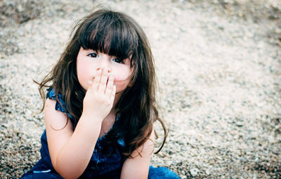 High angle portrait of girl covering mouth while sitting on field