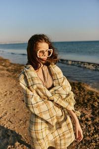 Young woman standing at beach against sky during sunset