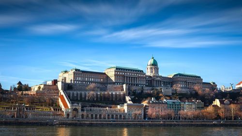 Buildings by river against cloudy sky