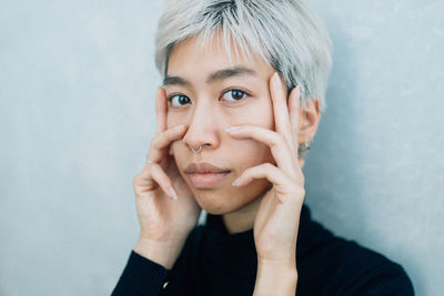 Portrait of woman touching cheek against wall