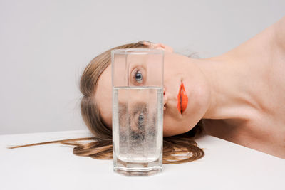 Beautiful woman looking through glass water looks into camera, bright orange