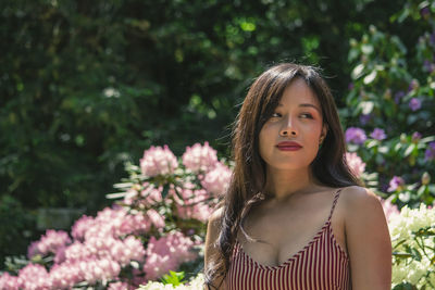 Portrait of a beautiful young woman standing by flowering plants