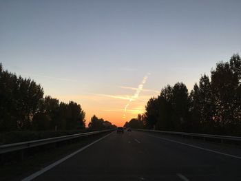 Road amidst silhouette trees against sky during sunset