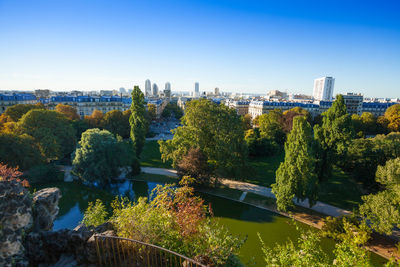 Plants and trees by buildings against blue sky