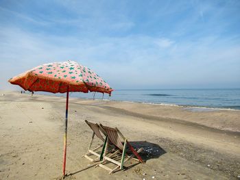 Deck chairs on shore at beach against sky