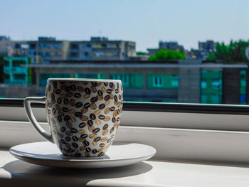 Close-up of coffee cup on table by balcony against sky