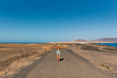 Rear view of woman standing on land against clear blue sky