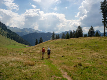 Rear view of men walking on field against sky