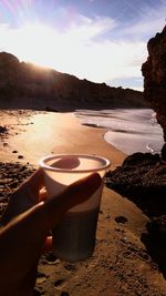 Hand holding sand at beach against sky during sunset