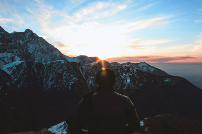 Rear view of man looking at mountains against sky