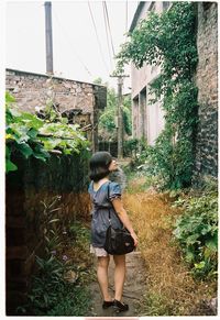 Rear view of woman standing by plants against building