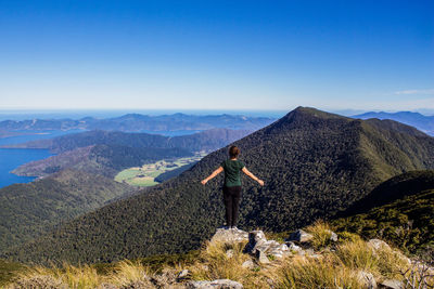 Rear view of woman with arms outstretched standing on mountain against sky