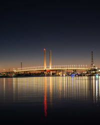 Illuminated city by river against sky at night