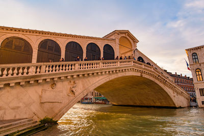 Arch bridge over river against cloudy sky