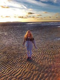 Woman standing on beach against sky during sunset