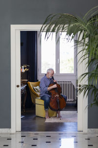 Senior man playing cello while sitting at home