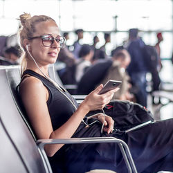 Smiling woman using smart phone sitting at airport