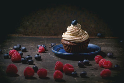 Close-up of chocolate cupcake with whipped cream by berries on table
